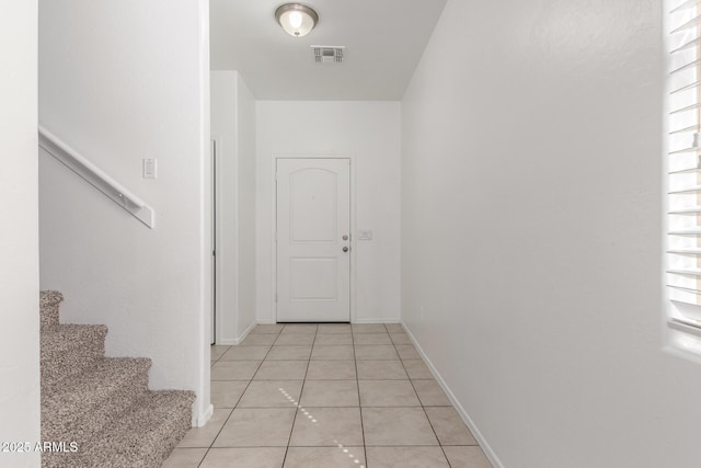 doorway with light tile patterned floors, visible vents, baseboards, and stairs