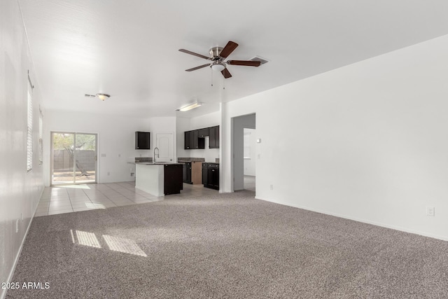 unfurnished living room with light tile patterned floors, light colored carpet, a ceiling fan, a sink, and baseboards