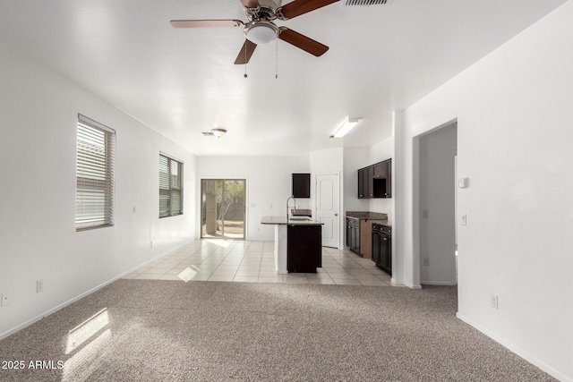 unfurnished living room with light tile patterned floors, light colored carpet, visible vents, ceiling fan, and a sink