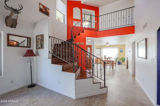 stairs with tile patterned flooring, a towering ceiling, and ceiling fan