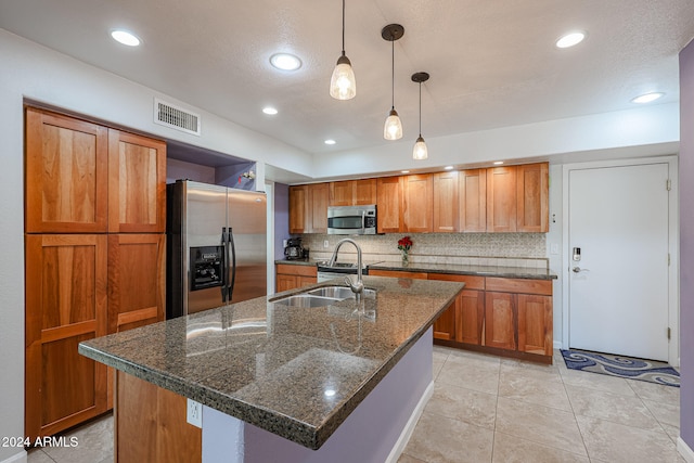 kitchen featuring hanging light fixtures, dark stone countertops, stainless steel appliances, and a kitchen island with sink