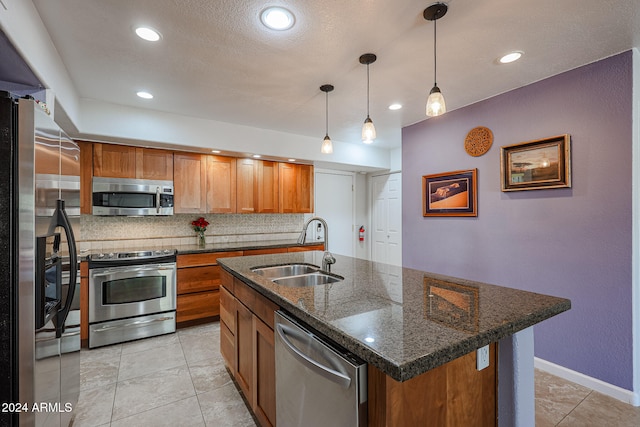 kitchen with sink, dark stone counters, decorative light fixtures, a center island with sink, and appliances with stainless steel finishes