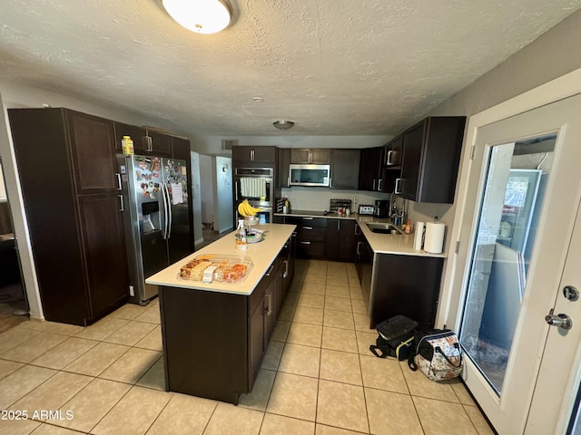 kitchen featuring a kitchen island, light tile patterned flooring, a sink, light countertops, and appliances with stainless steel finishes