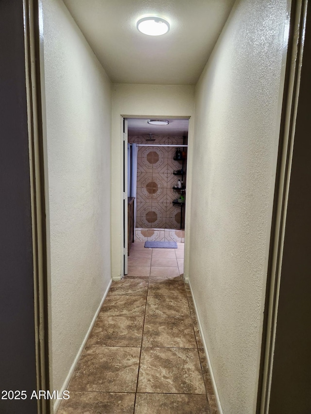 corridor featuring baseboards, tile patterned flooring, and a textured wall