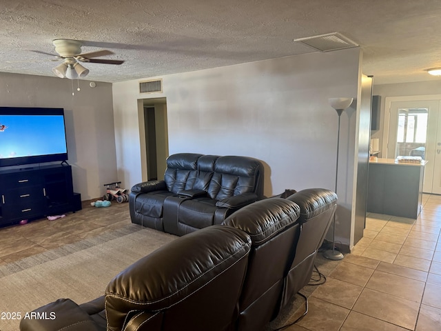 living room featuring tile patterned floors, visible vents, a textured ceiling, and a ceiling fan