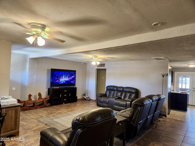 living room featuring light tile patterned floors, visible vents, a textured ceiling, and ceiling fan