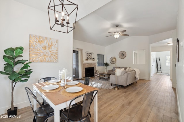 dining room featuring ceiling fan, lofted ceiling, a stone fireplace, and light wood-type flooring