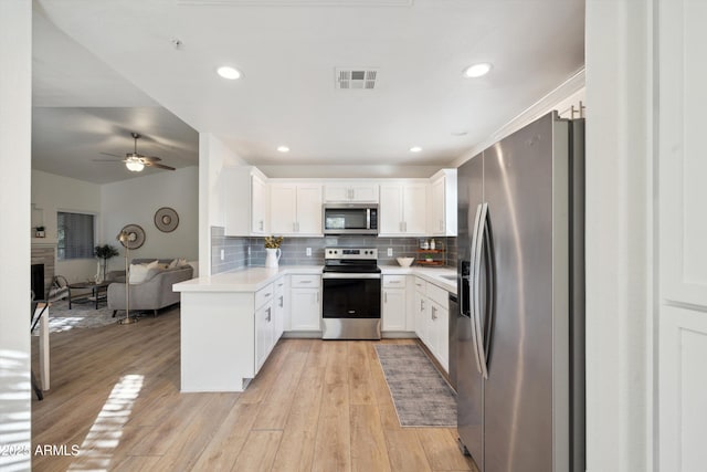 kitchen with stainless steel appliances, kitchen peninsula, a brick fireplace, and white cabinets