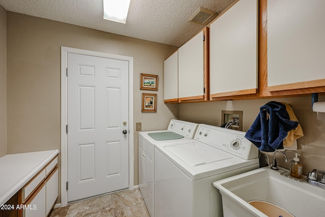 clothes washing area featuring washer and clothes dryer, cabinets, sink, and a textured ceiling