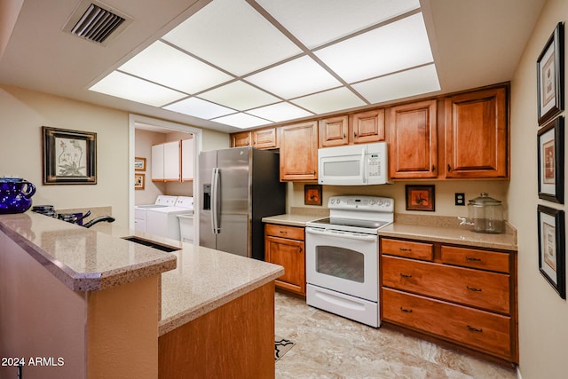 kitchen featuring light stone countertops, white appliances, sink, kitchen peninsula, and washing machine and clothes dryer