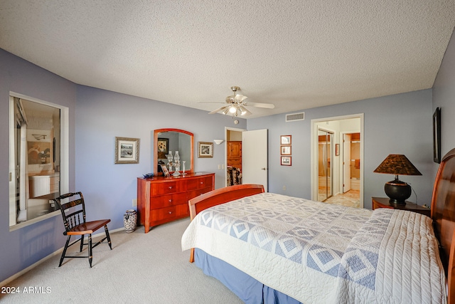 bedroom with ceiling fan, light colored carpet, a textured ceiling, and connected bathroom