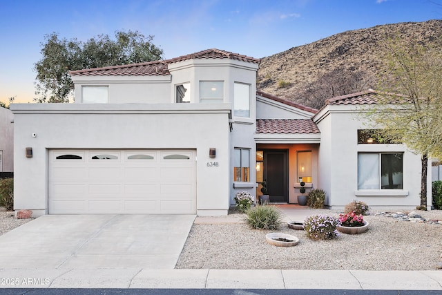 mediterranean / spanish home with a garage, concrete driveway, a tile roof, and stucco siding