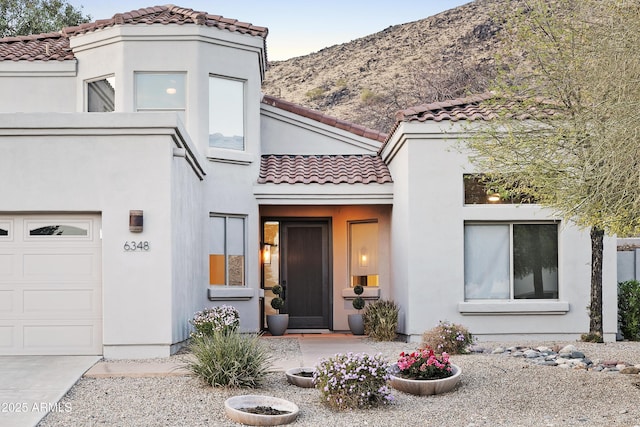 view of front of property featuring an attached garage, a tile roof, a mountain view, and stucco siding