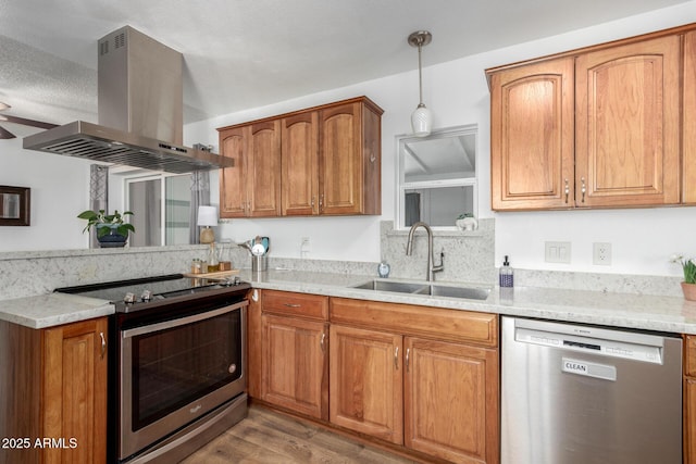 kitchen with sink, pendant lighting, island exhaust hood, stainless steel appliances, and light stone countertops