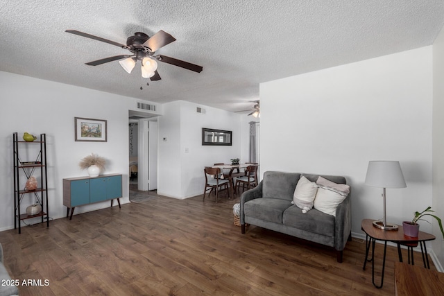 living room with dark wood-type flooring, ceiling fan, and a textured ceiling