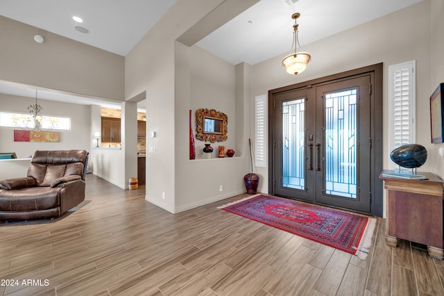 entrance foyer with french doors, light hardwood / wood-style floors, and an inviting chandelier