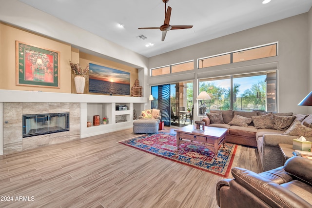 living room with a tiled fireplace, ceiling fan, built in shelves, and hardwood / wood-style flooring