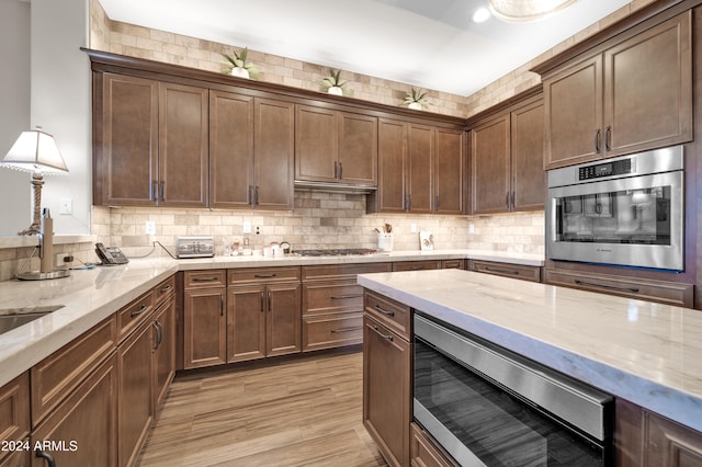 kitchen featuring light stone countertops, appliances with stainless steel finishes, tasteful backsplash, and light hardwood / wood-style flooring