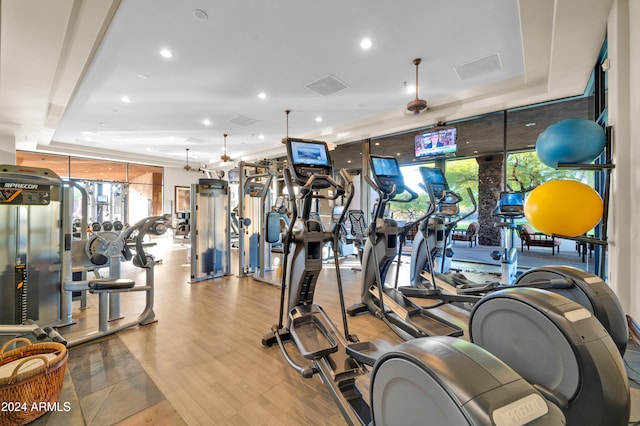 gym featuring light wood-type flooring, a raised ceiling, and ceiling fan