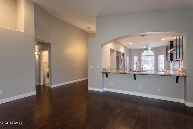 kitchen with light stone counters, dark hardwood / wood-style floors, stainless steel refrigerator, washer / dryer, and kitchen peninsula