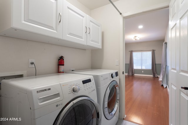 clothes washing area featuring hardwood / wood-style floors, cabinets, and washer and dryer