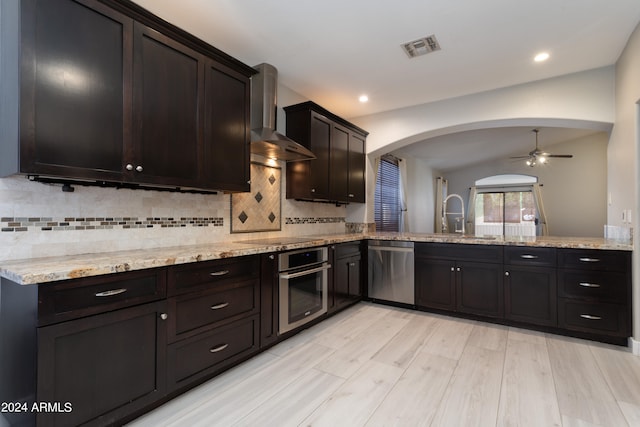 kitchen featuring stainless steel appliances, decorative backsplash, wall chimney exhaust hood, sink, and light stone countertops