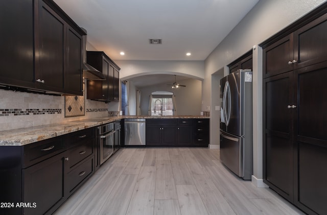 kitchen featuring appliances with stainless steel finishes, dark brown cabinets, light stone countertops, tasteful backsplash, and ceiling fan