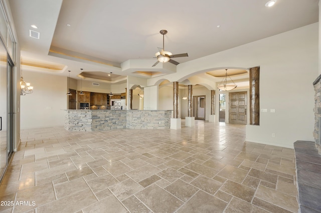 unfurnished living room featuring ceiling fan with notable chandelier and a raised ceiling