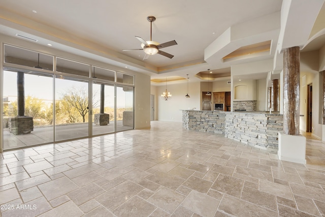 unfurnished living room with a tray ceiling and ceiling fan with notable chandelier