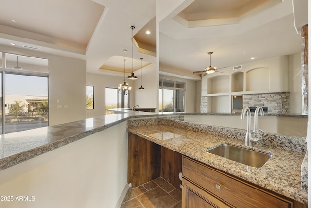 kitchen featuring a tray ceiling, light stone counters, sink, and ceiling fan with notable chandelier