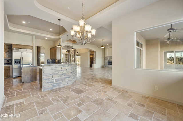 kitchen featuring ceiling fan with notable chandelier, a raised ceiling, stainless steel built in fridge, a fireplace, and decorative light fixtures