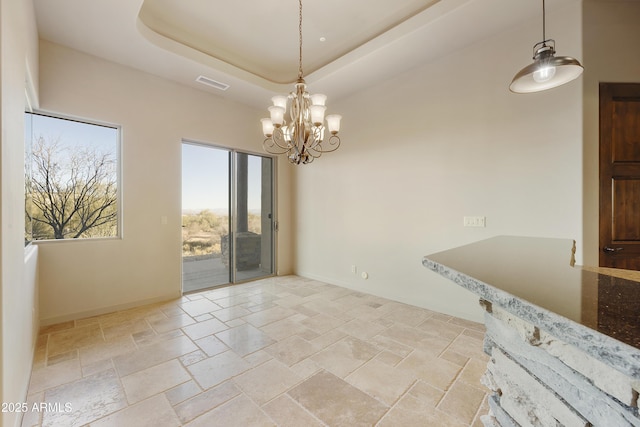 unfurnished dining area with a chandelier and a raised ceiling