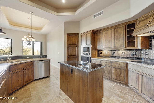 kitchen with sink, a raised ceiling, decorative light fixtures, a center island with sink, and appliances with stainless steel finishes