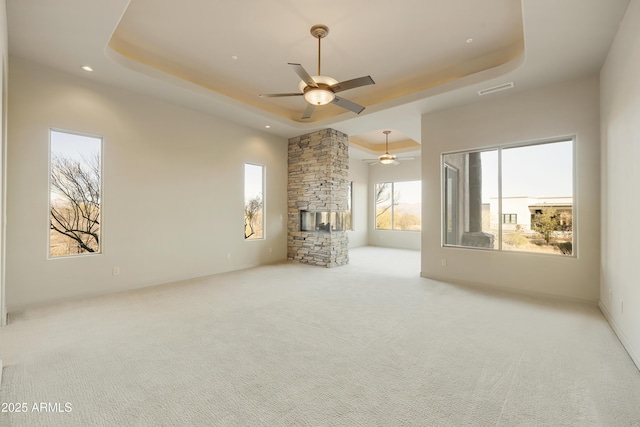 unfurnished living room featuring a raised ceiling, a stone fireplace, ceiling fan, and light colored carpet