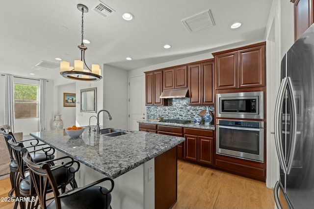 20701 W Minnezona Ave, Buckeye, AZ 85396 - kitchen featuring light wood-type flooring, a sink, under cabinet range hood, a kitchen breakfast bar, and stainless steel appliances