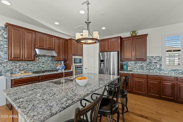 20701 W Minnezona Ave, Buckeye, AZ 85396 - kitchen featuring a breakfast bar area, a sink, stainless steel appliances, under cabinet range hood, and light wood-type flooring