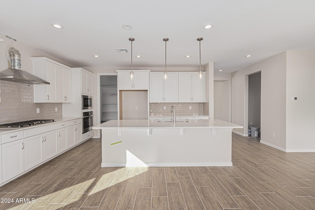 kitchen with white cabinetry, light hardwood / wood-style floors, stainless steel appliances, and a center island with sink