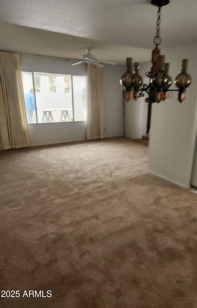 carpeted spare room featuring ceiling fan with notable chandelier