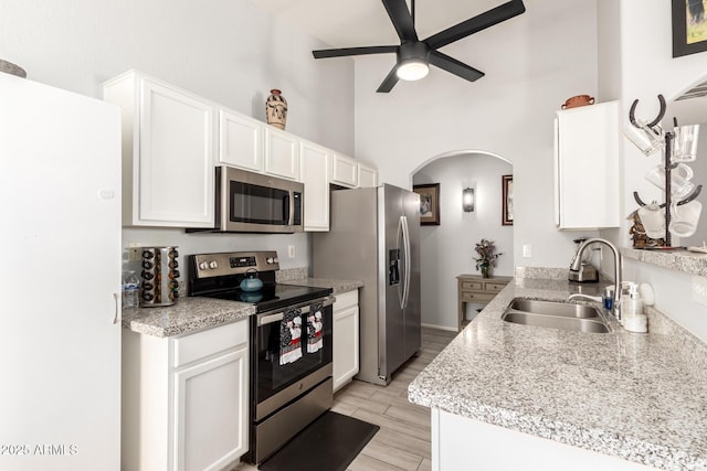 kitchen with arched walkways, a ceiling fan, white cabinetry, appliances with stainless steel finishes, and a sink