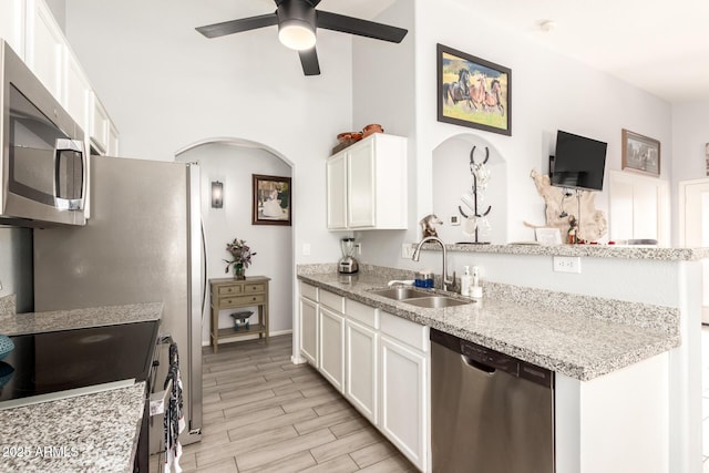 kitchen featuring a ceiling fan, white cabinets, appliances with stainless steel finishes, arched walkways, and a sink