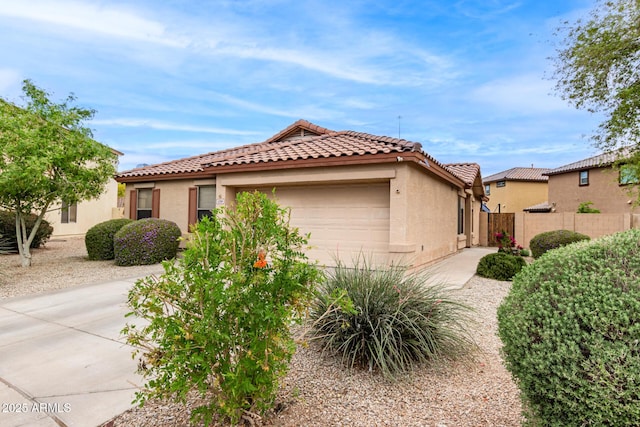 mediterranean / spanish house featuring concrete driveway, stucco siding, an attached garage, a tiled roof, and fence