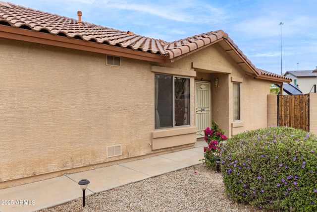 exterior space featuring fence, stucco siding, visible vents, and a tile roof