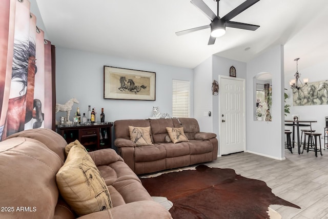 living area featuring ceiling fan with notable chandelier, light wood-style flooring, arched walkways, vaulted ceiling, and baseboards