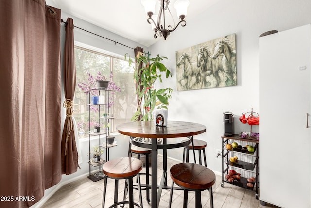dining area with light wood finished floors, a notable chandelier, vaulted ceiling, and baseboards
