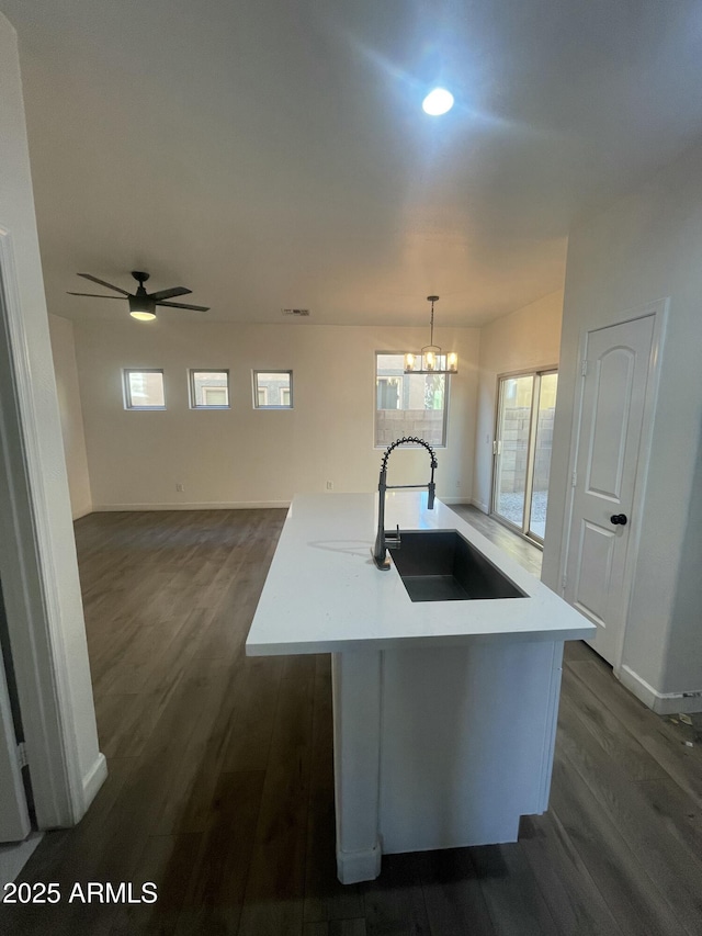 kitchen featuring sink, decorative light fixtures, ceiling fan with notable chandelier, a center island with sink, and dark wood-type flooring