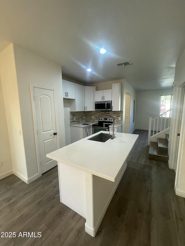 kitchen featuring tasteful backsplash, a kitchen island with sink, dark hardwood / wood-style flooring, white cabinets, and appliances with stainless steel finishes