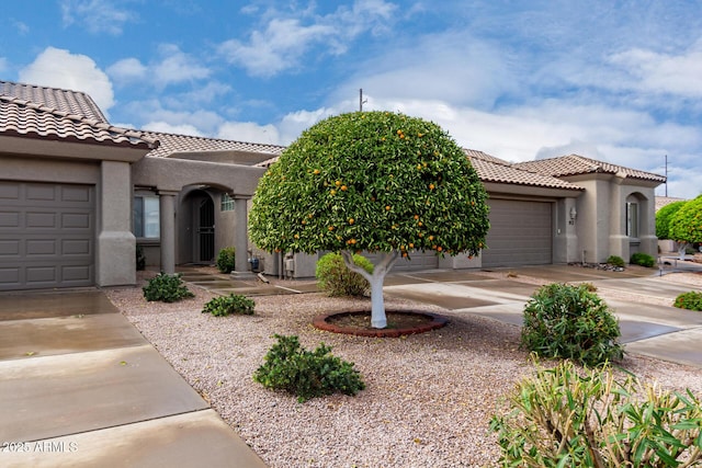 mediterranean / spanish-style home featuring stucco siding, an attached garage, a tile roof, and driveway