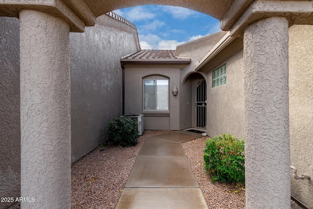 view of exterior entry with stucco siding, central AC, and a tile roof