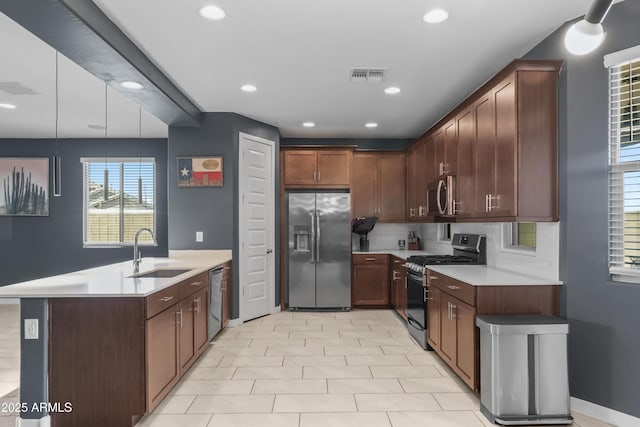 kitchen featuring visible vents, a peninsula, stainless steel appliances, light countertops, and a sink