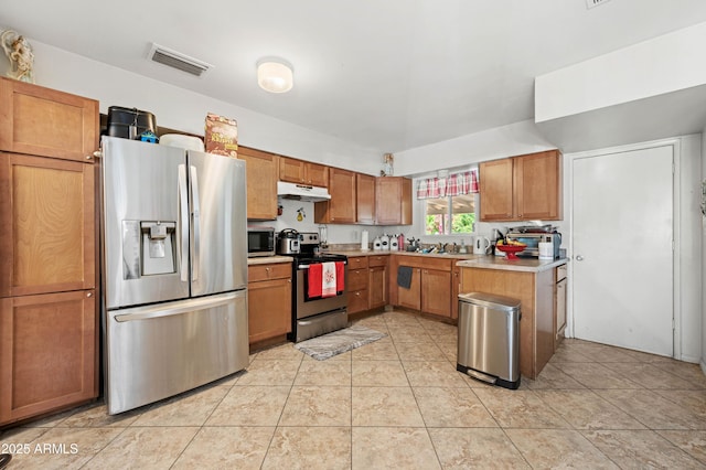 kitchen with light countertops, under cabinet range hood, visible vents, brown cabinets, and appliances with stainless steel finishes